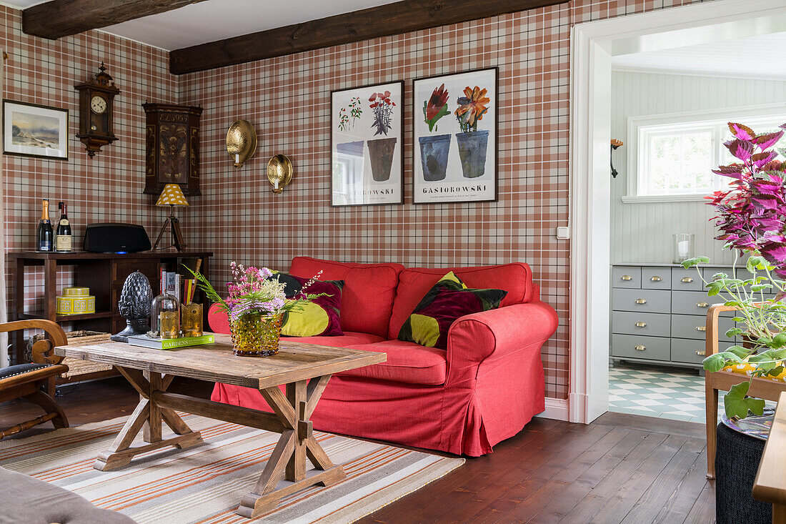Wohnzimmer mit rotem Hussensofa, Holztisch und karierter Tapete