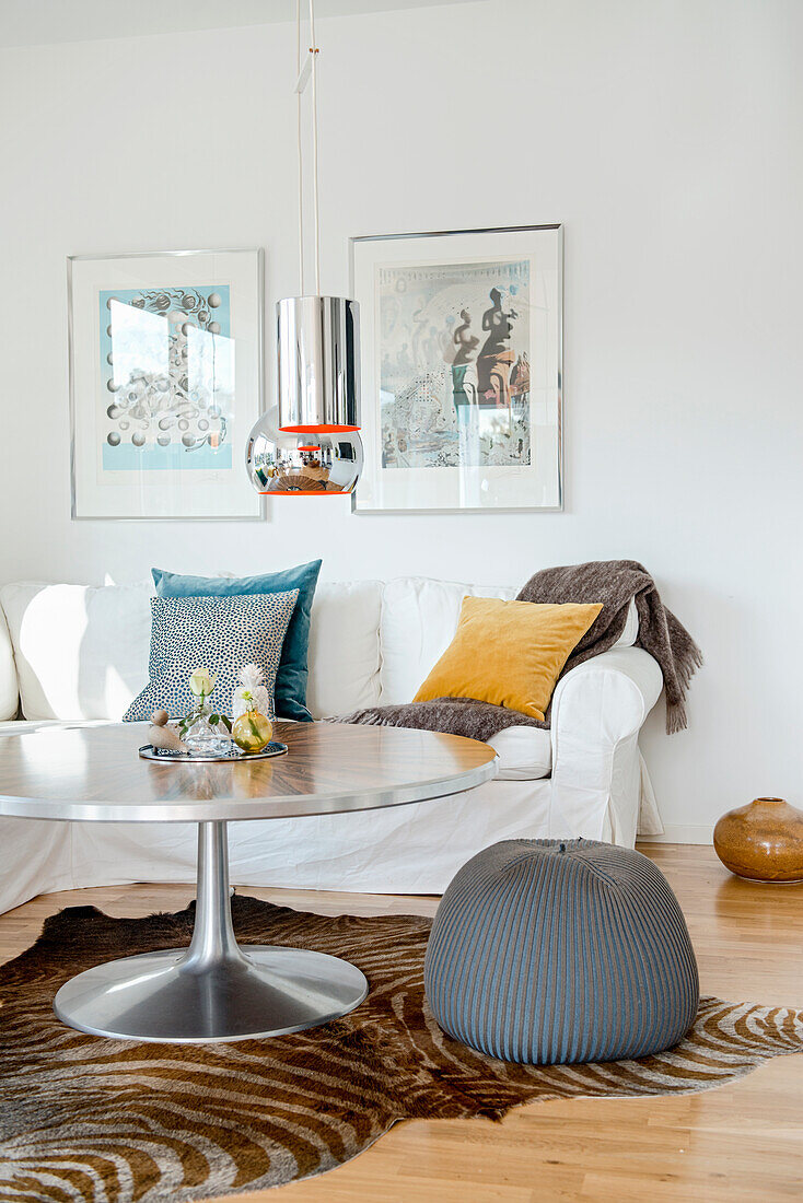 Weißes Hussensofa mit Kissen und runder Tisch mit Sitzpouf auf Zebrafell im Wohnzimmer