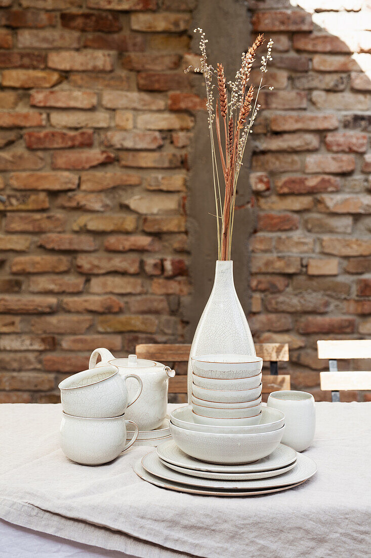 Keramikgeschirr und Vase mit Getreideähren auf Tisch im Freien