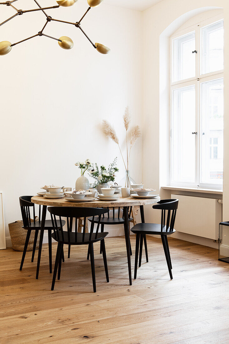 Gedeckter runder Tisch mit schwarzen Stühlen vor Fenster in Altbauwohnung