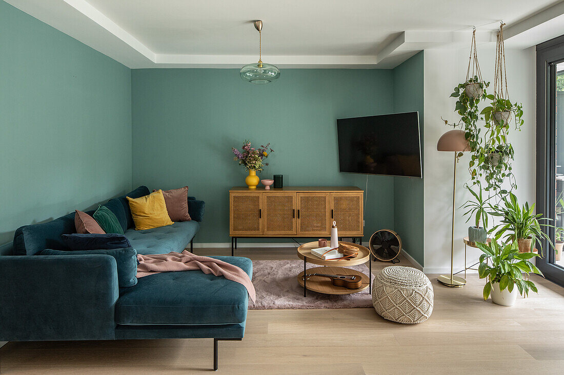 Ecksofa, Lowboard, Fernseher und Topfpflanzen im Wohnzimmer mit grünen Wänden