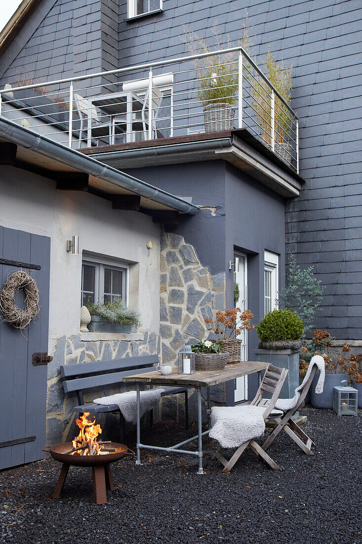 Terrasse mit Feuerstelle und Sitzgelegenheiten vor einem Haus in Grautönen