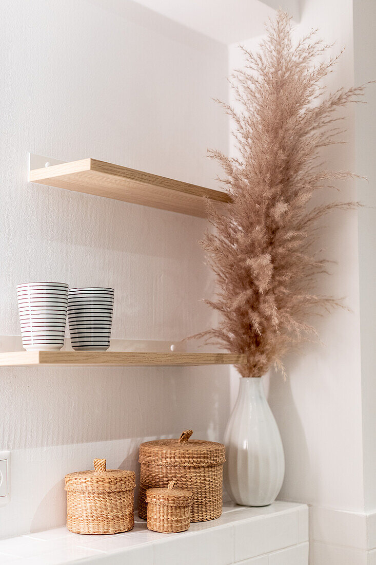 Weiße Ablage mit Körbchen und Trockengras in Vase, darüber Holzregale im Bad