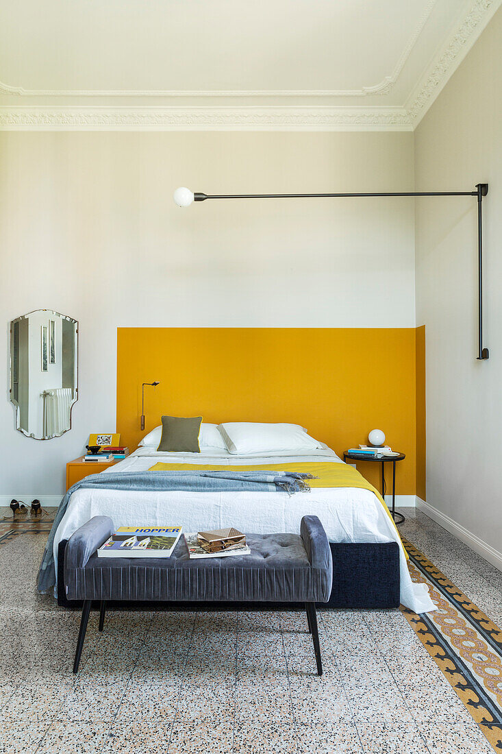 Gepolsterte Kleiderbank und Doppelbett vor gelber Wand im Schlafzimmer