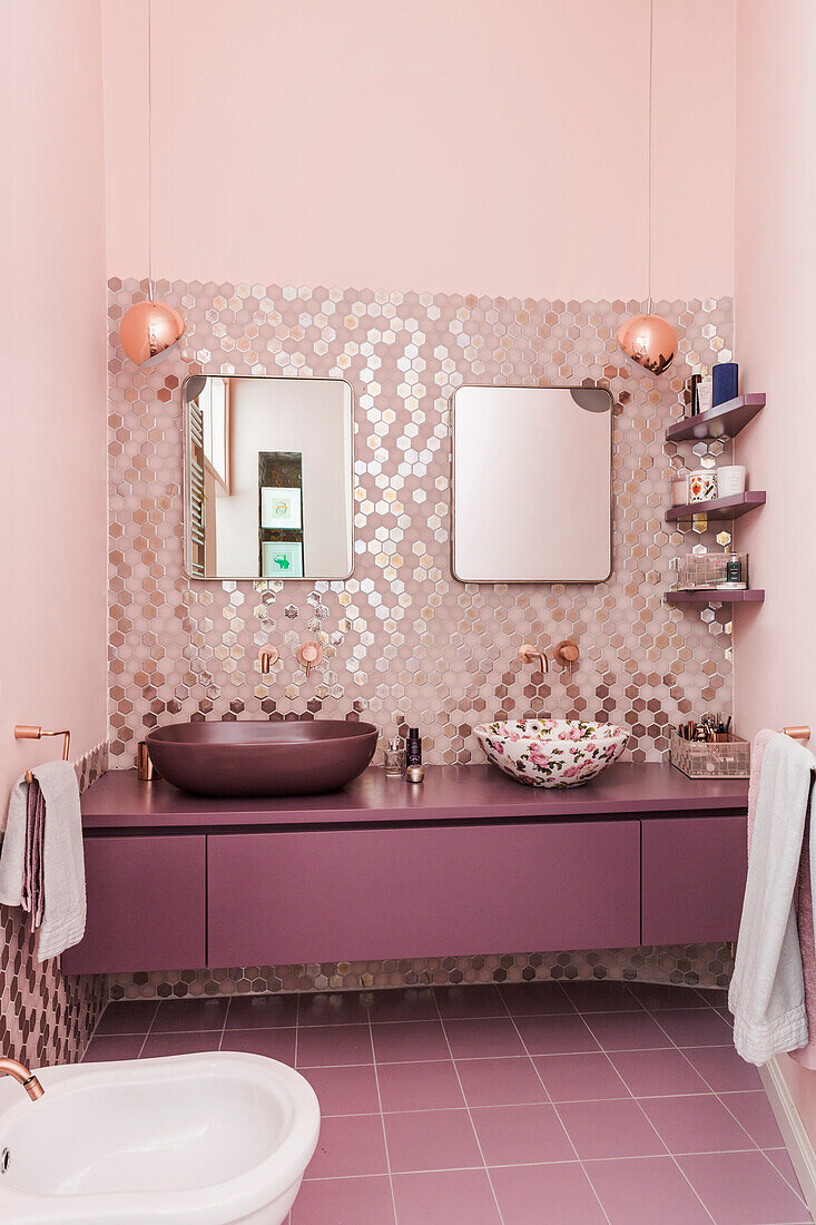 Washstand with twin sinks against glass mosaic in bathroom in shades of pink