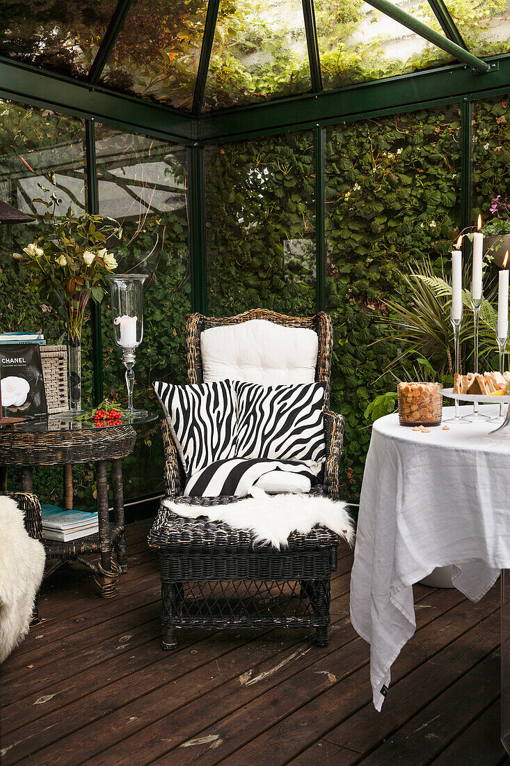 Runder, gedeckter Tisch, Sessel mit Kissen in Animal-Print und Fußschemel im Wintergarten