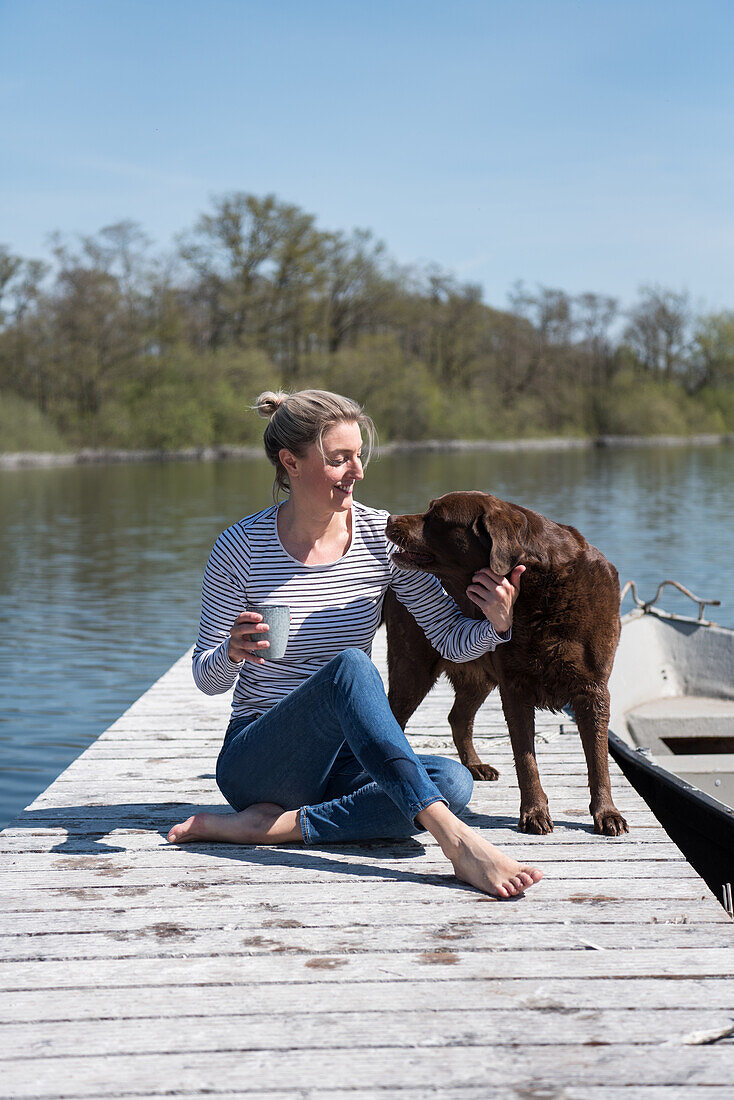 Blonde woman and dog sitting on wooden jetty