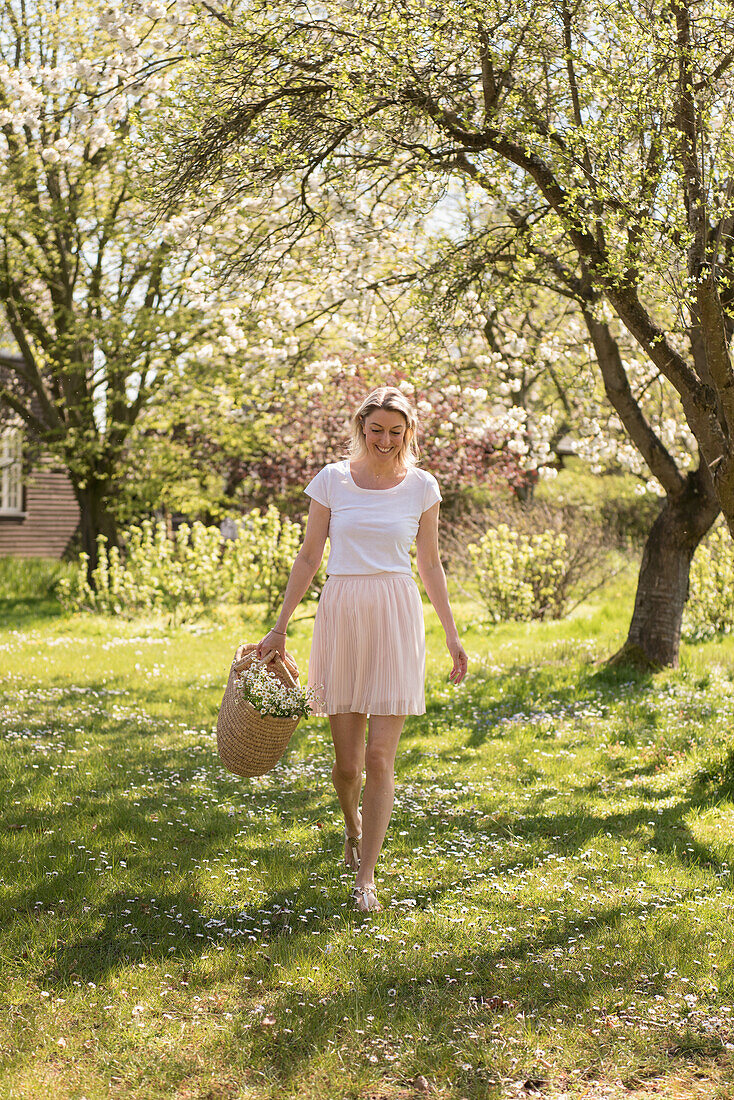 Blonde woman wearing white t-shirt and skirt with basket of flowers in spring garden