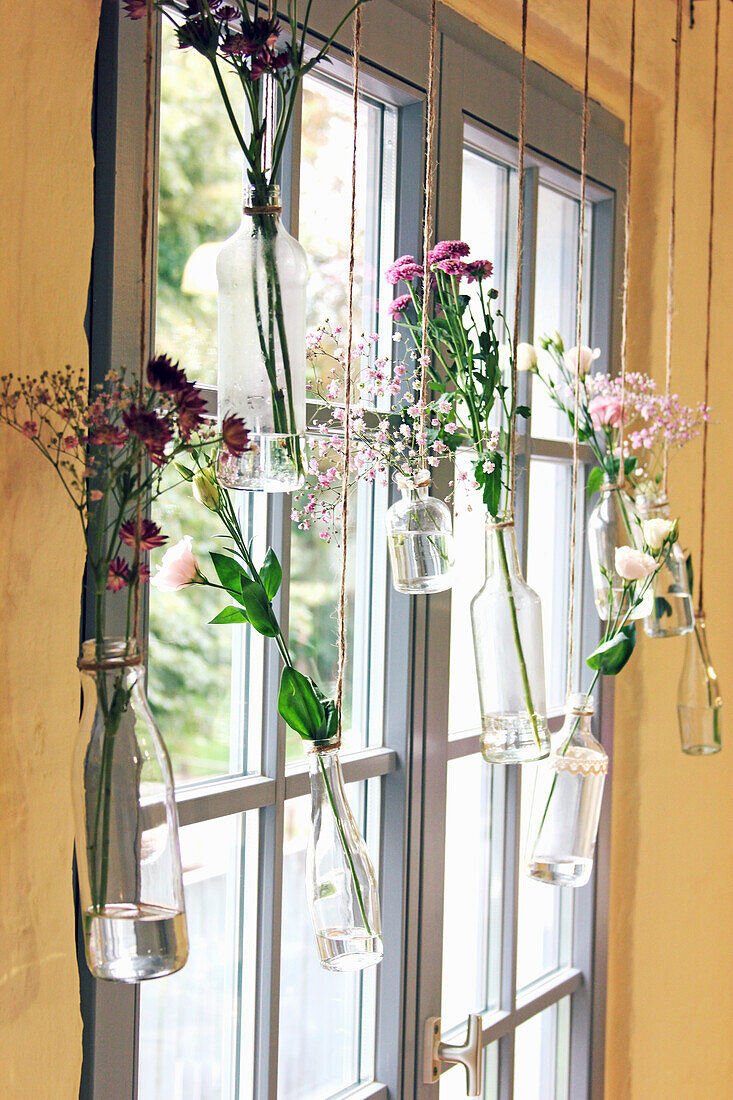 Suspended vases of flowers in window