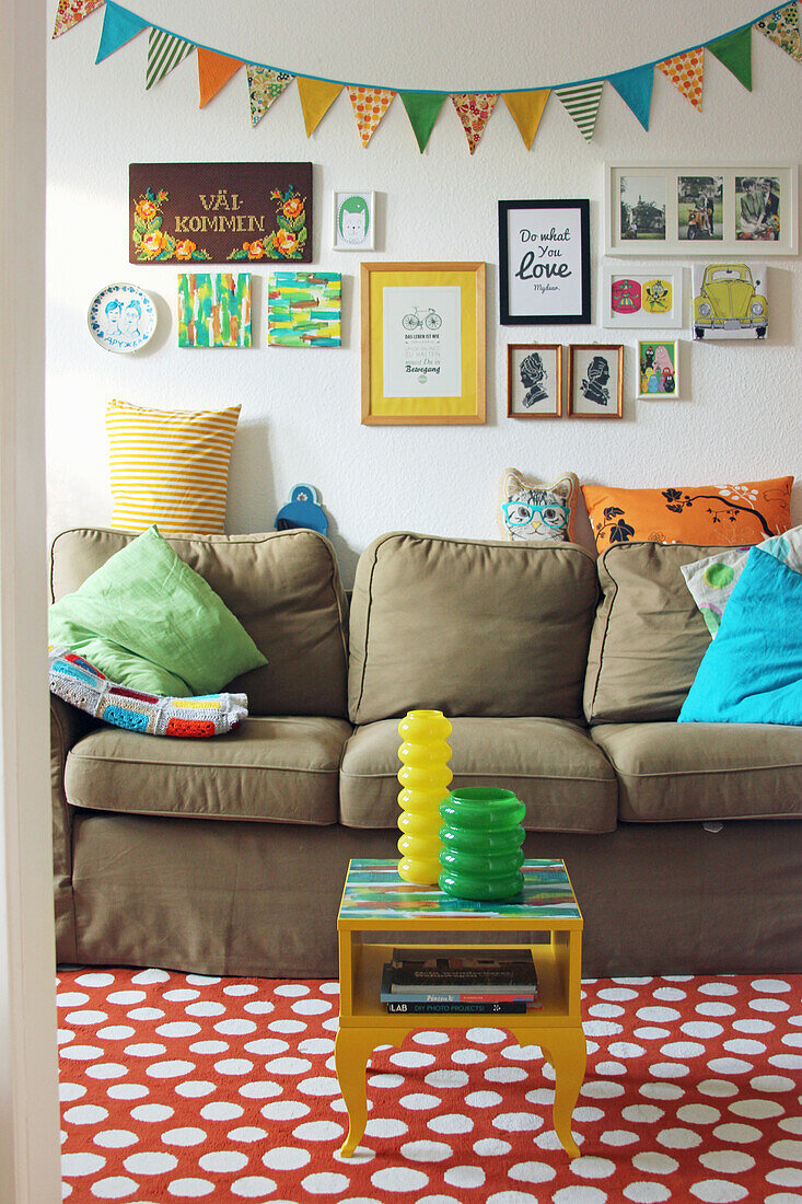 Sofa mit Kissen, Bilder und Wimpelkette an der Wand, Tischchen auf gepunktetem Teppich
