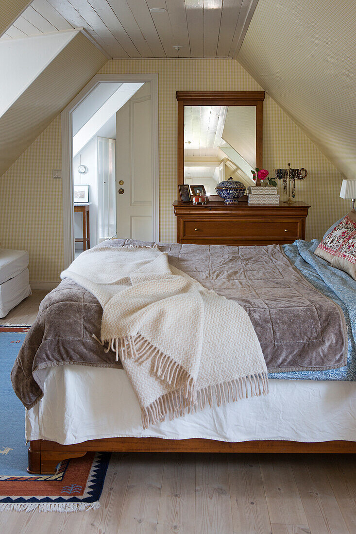 King size bed, wooden bureau, with a wall mounted mirror in the bedroom with sloping roof