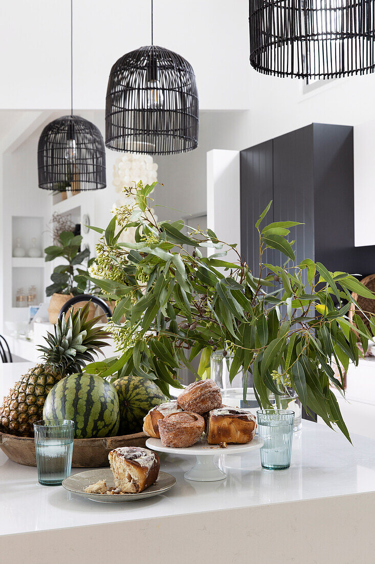Pastries, fruit bowl and leafy branches on kitchen island