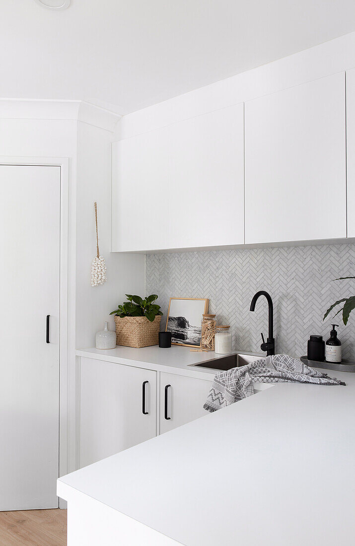 White fitted kitchen cabinets over corner with tiles in herringbone pattern