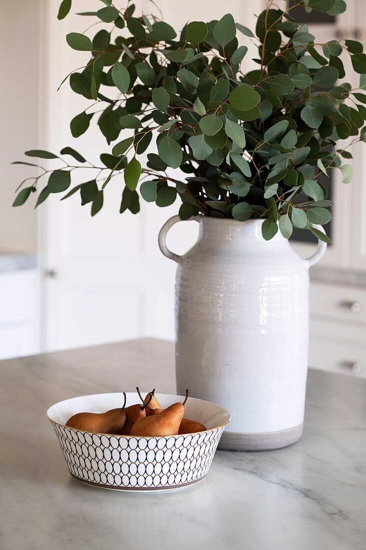 Bowl with pears and ceramic vase with eucalyptus branches on kitchen table