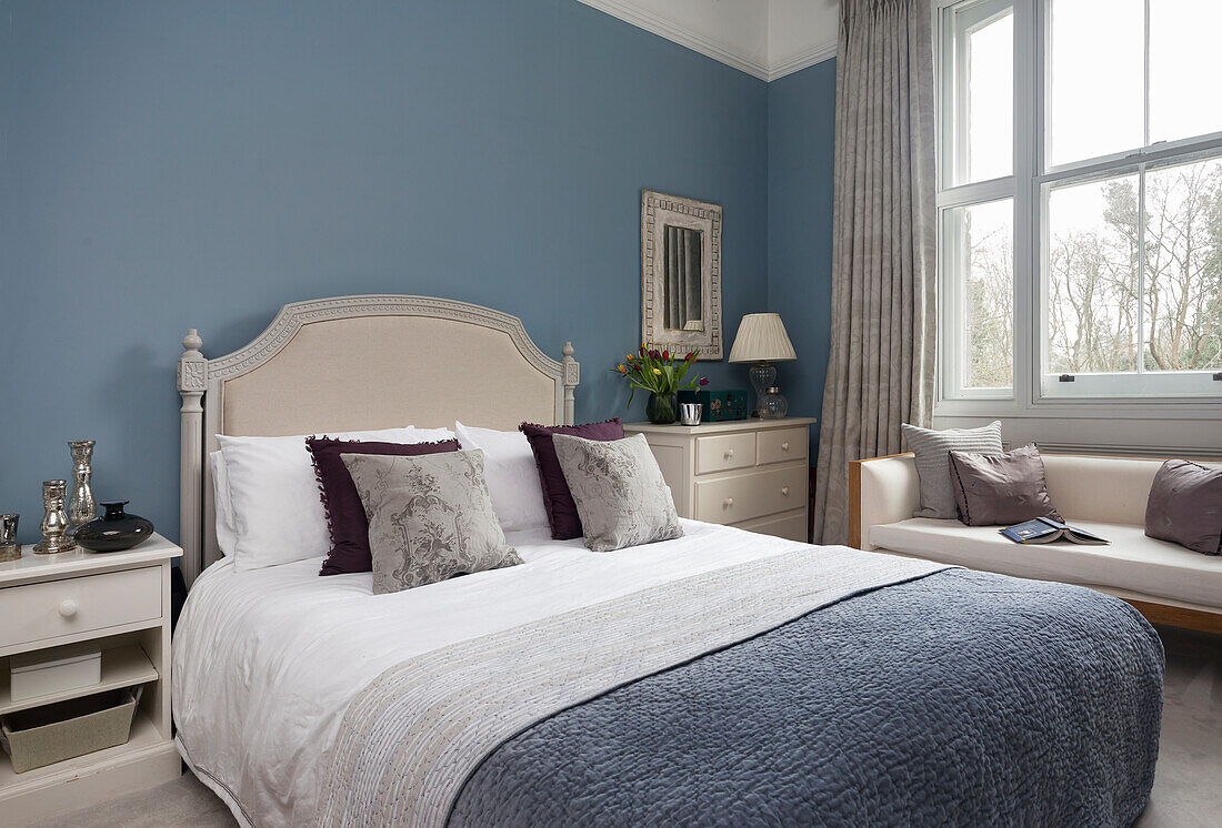Double bed with headboard and sofa in cream shades in guest bedroom with blue walls
