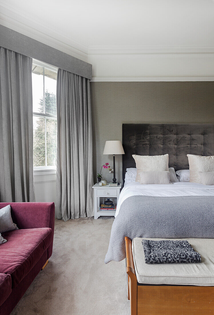 Elegant bedroom with double bed in shades of grey and claret sofa