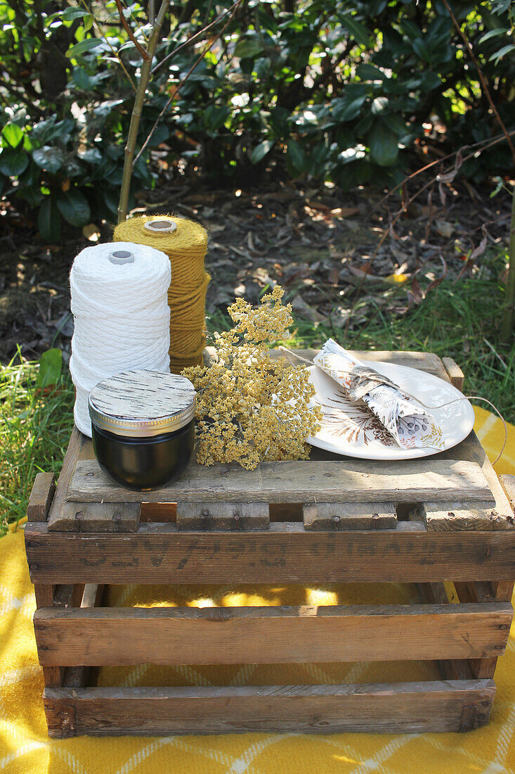 Garnrollen, Marmeladenglas, Blüte, Teller und Serviette auf Holzkiste