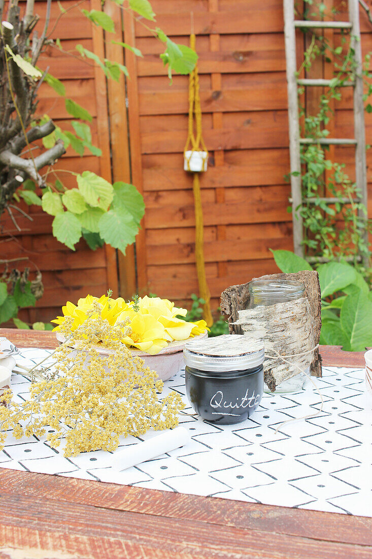 Marmeladenglas mit DIY-Deckel aus Birkenrinde und Blüten auf Tisch