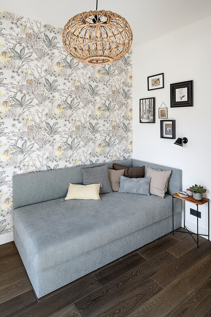 Grey upholstered sofa bed against wall with patterned wallpaper