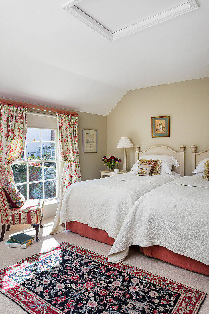 Guest bedroom with twin beds against beige wall and lattice window with floral curtains