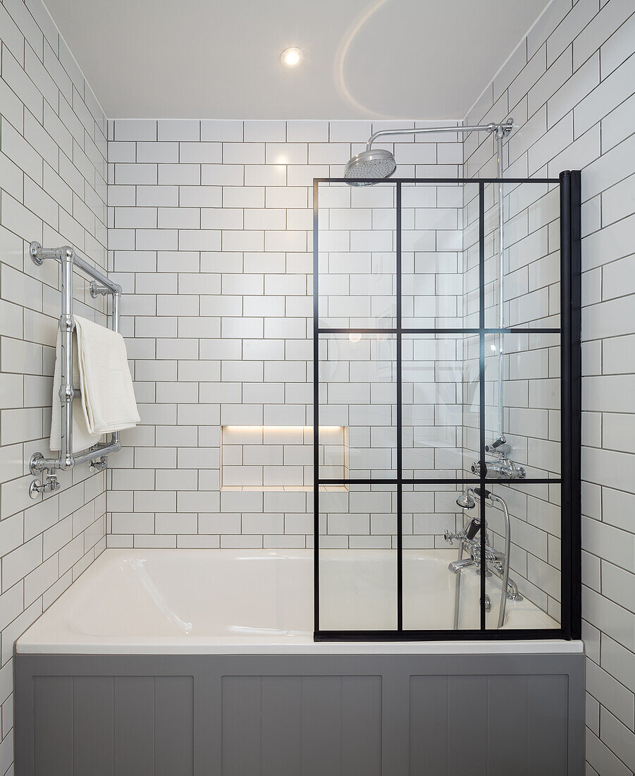 Bathtub with shower screen in white-tiled bathroom