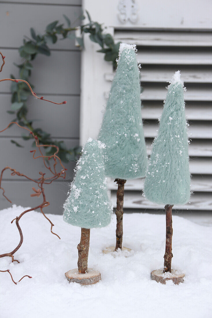 Three decorative, snow-covered miniature Christmas trees made of felt on wooden trunks