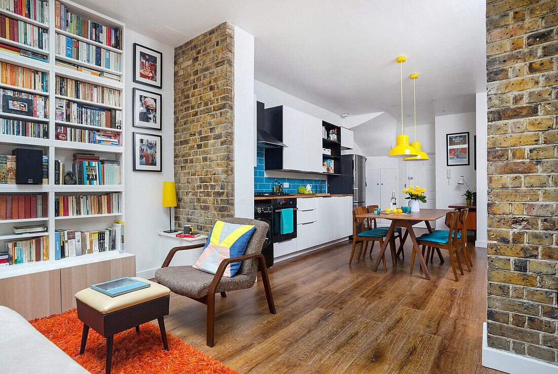 Floor-to-ceiling shelves, retro armchair and footstool in open-plan interior with reclaimed brick wall