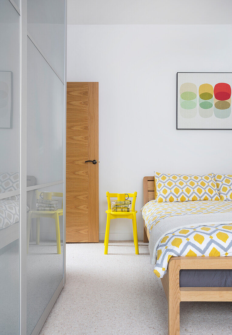 Double bed, yellow chair and tall wardrobe with sliding glass doors in bedroom