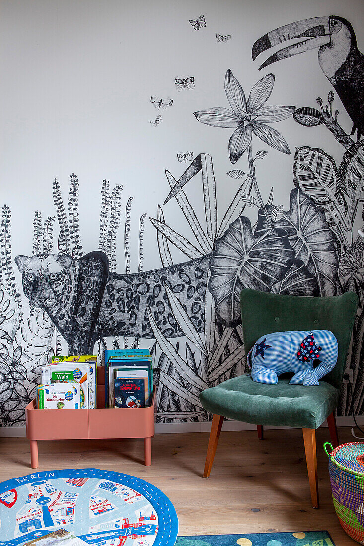 Bookcase and upholstered chair against wallpaper with jungle motif in child's bedroom