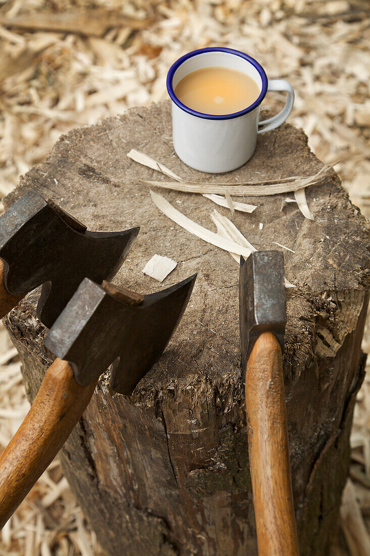 Axes in a tree trunk and a mug of tea in a carpenter's workshop