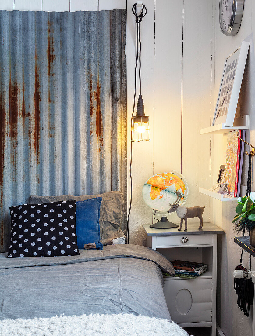 Bedroom corner with rustic metal wall decoration, bed, bedside table and hanging lamp