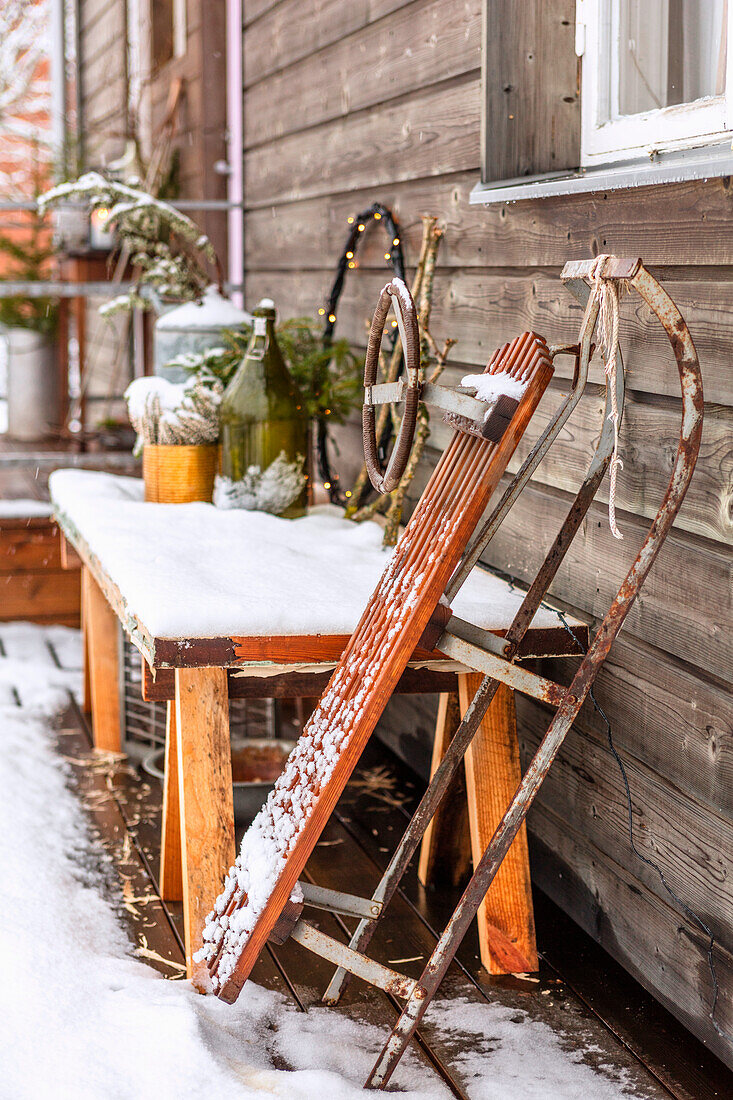 Winterliches Dekor und alter Holzschlitten im Schnee vor Holzhaus