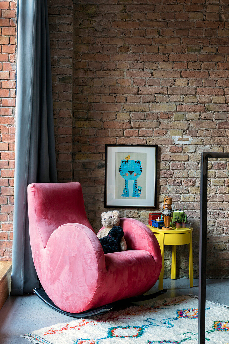 Pink armchair in front of red brick wall, yellow side table and patterned carpet