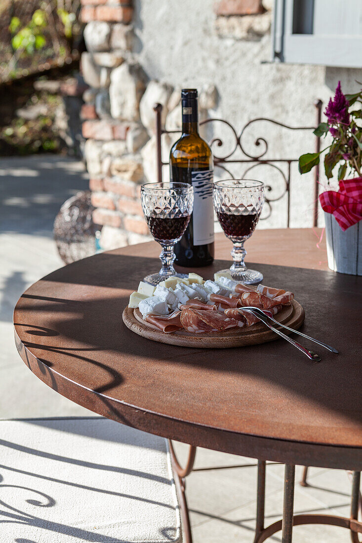 Flasche Wein, geriffelte Gläser und Holzplatte mit Antipasti im Garten