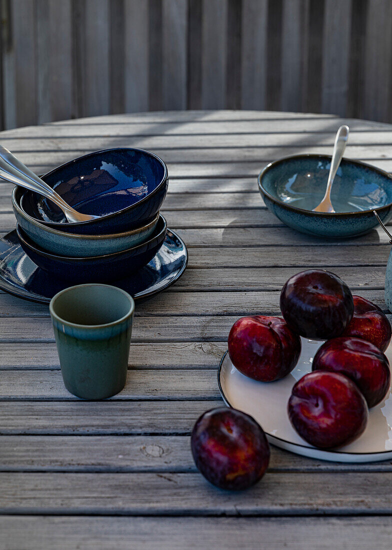 Red plums and blue ceramic tableware on a garden table