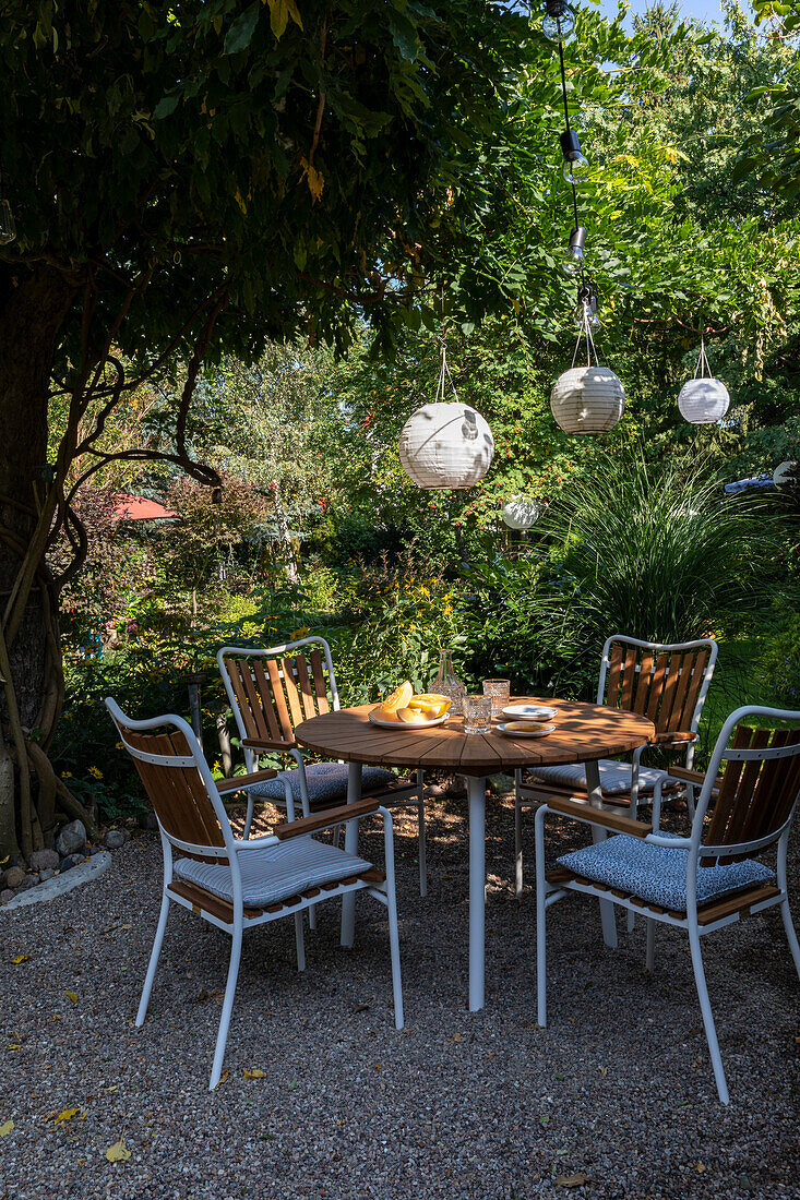 Round patio table with chairs on a gravel patio, lanterns above in garden