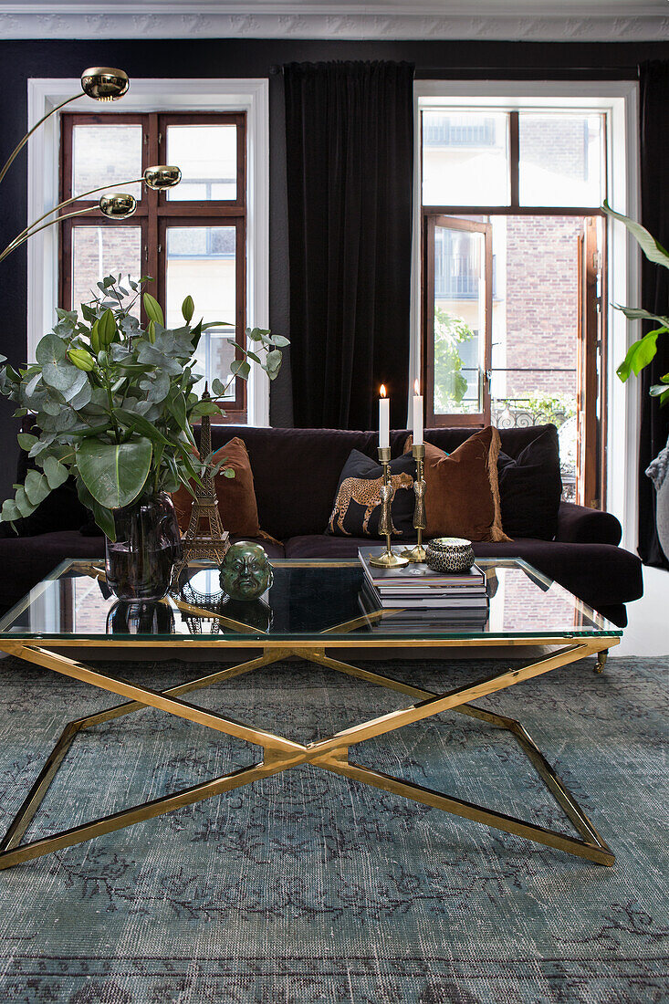 Living room with dark sofa, glass coffee table with golden frame and dark curtains