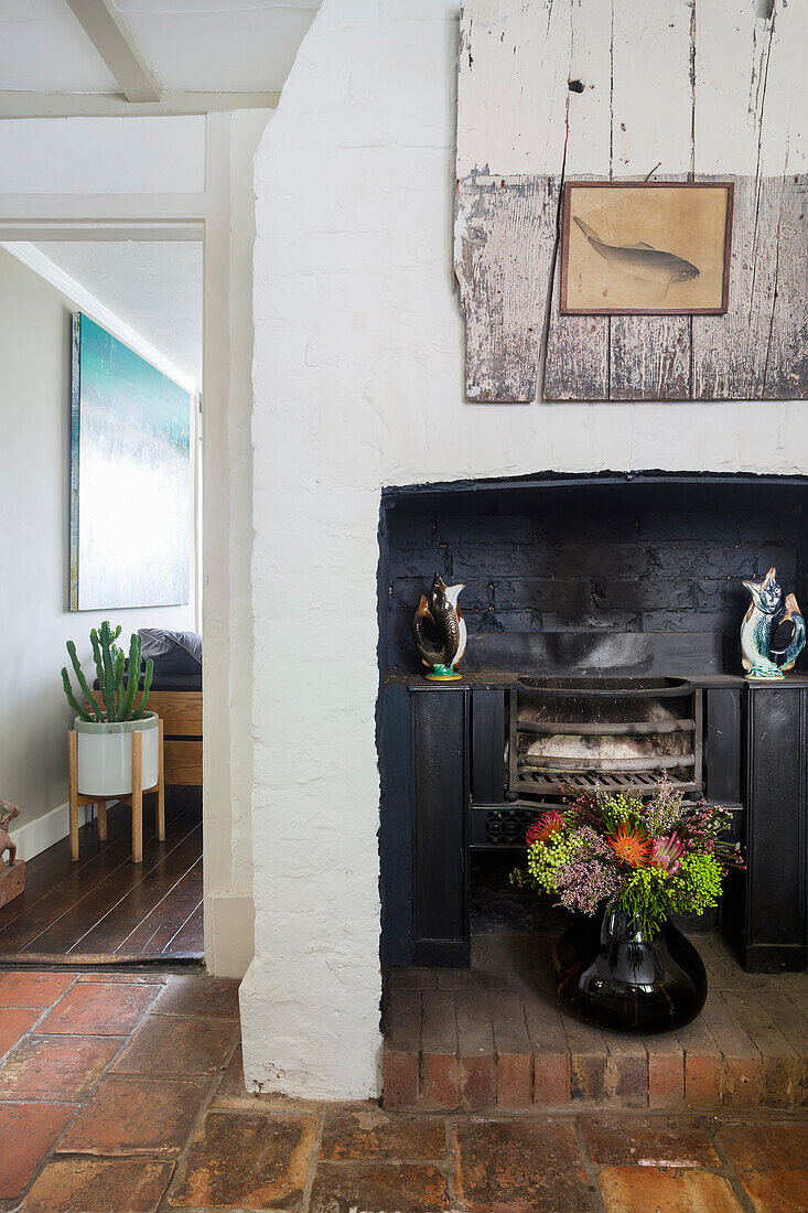 Rustic fireplace area with terracotta floor and vase of flowers