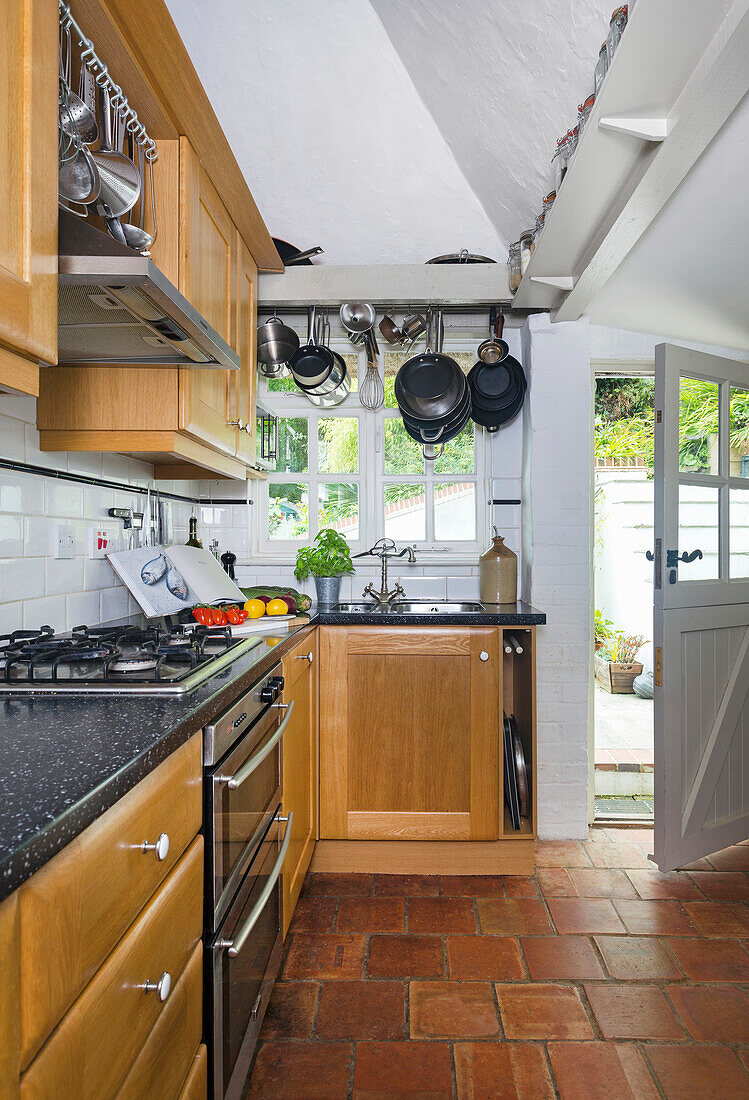Narrow kitchen with wooden cupboards and hanging rack for cookware