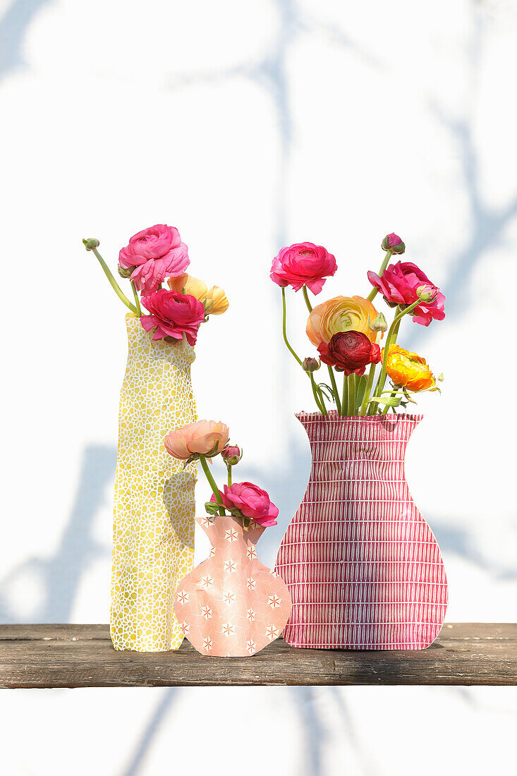 Ranunculus in glass vases covered artistically with paper in various vase shapes