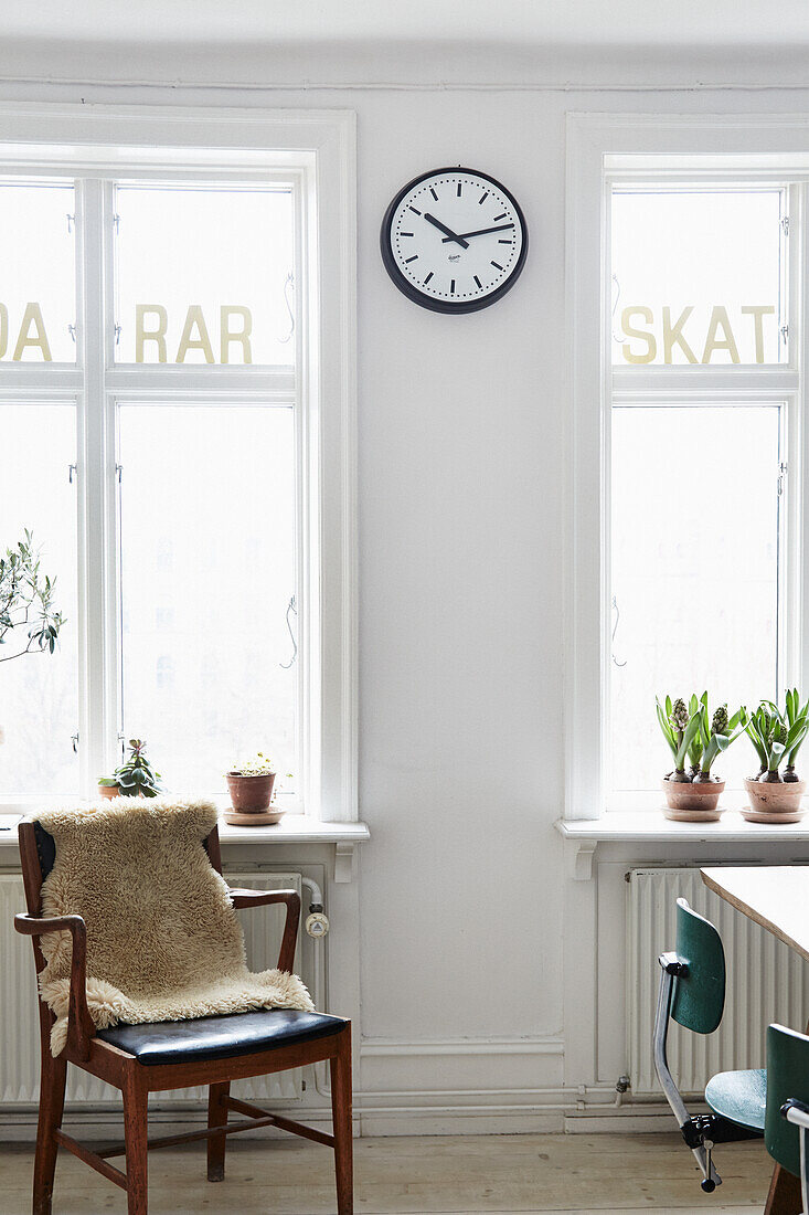 Wooden chair with fur throw in front of window sill with potted plants