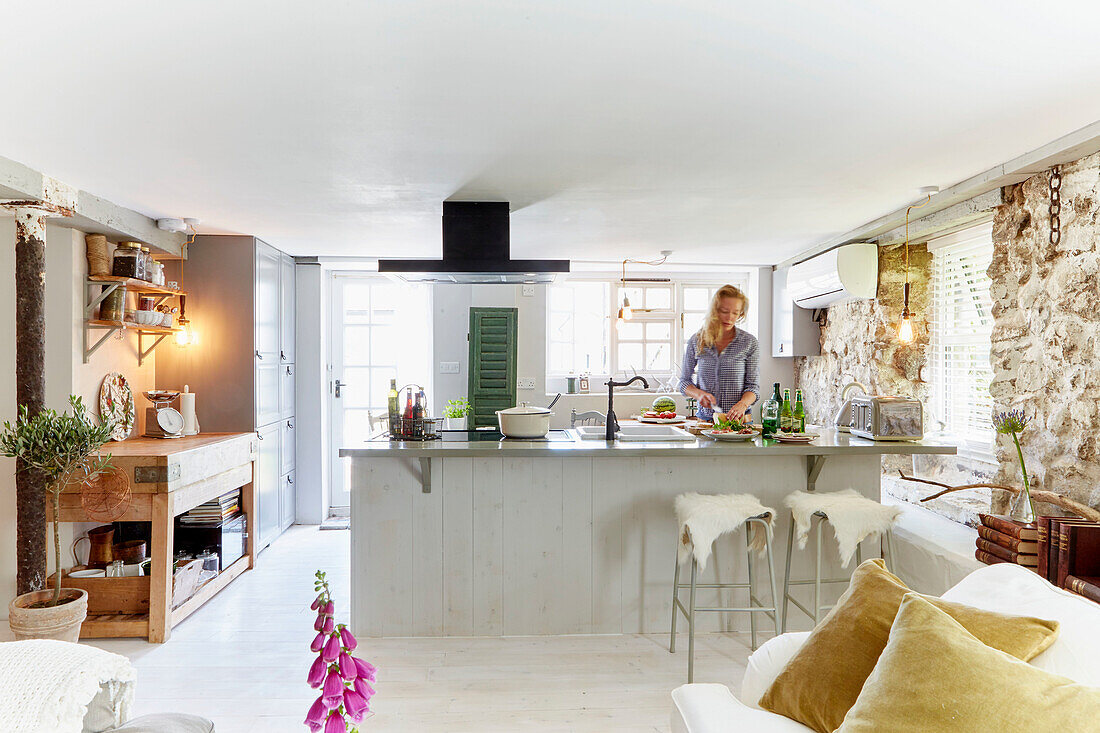 Woman in open country-style kitchen with large island and natural stone wall