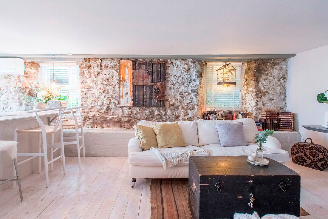 Living room with exposed stone, white sofa and dark wooden chest as a table