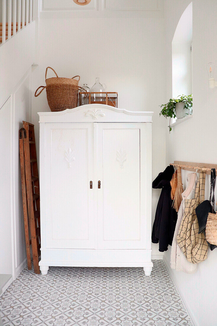 Weißer Vintageschrank mit Garderobe im Flur und gemusterten Bodenfliesen