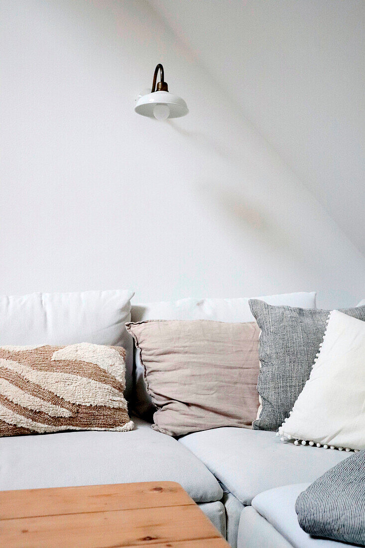White corner sofa with throw pillows and wall lamp in a minimalist style