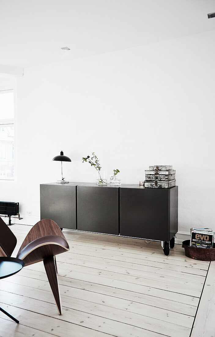 Schwarzes Sideboard vor weißer Wand und Klassikerstuhl aus Nussbaumholz im Wohnzimmer