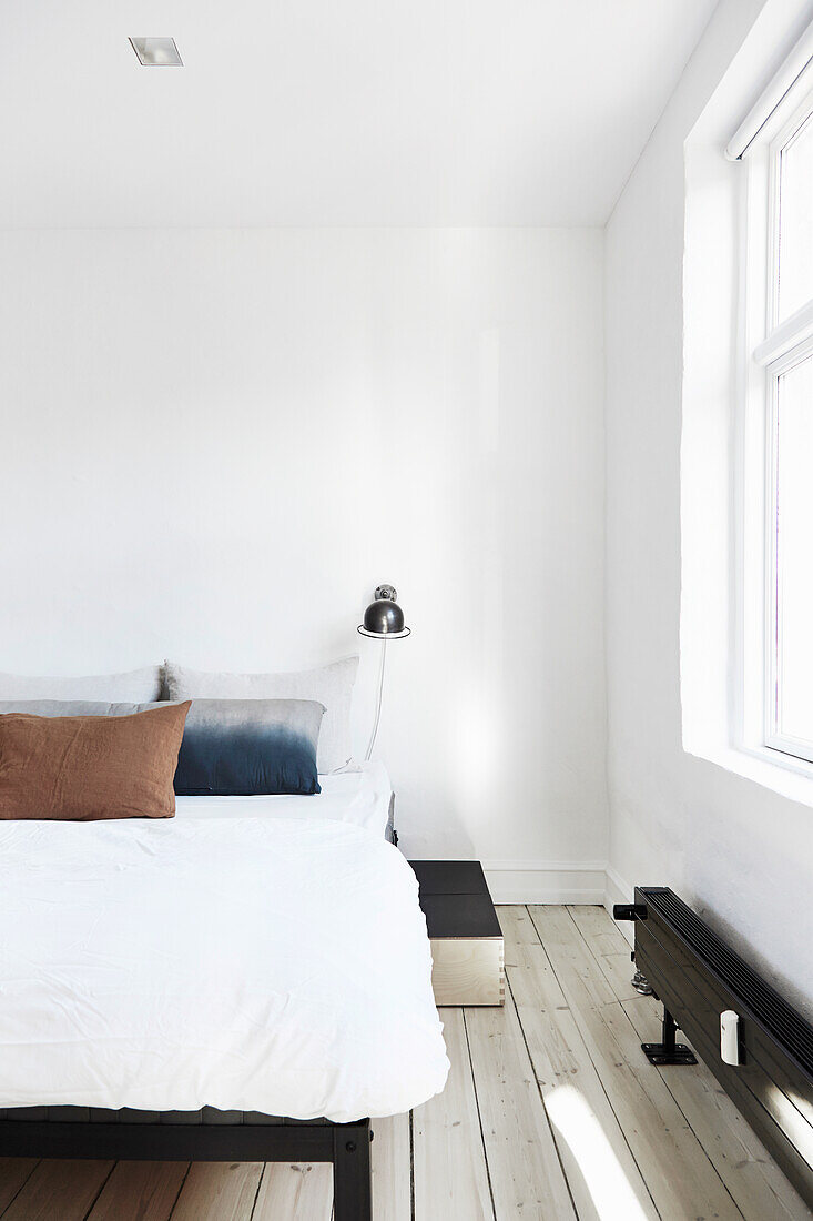 Doppelbett und Industrie-Leselampe in luftigem, weißem Schlafzimmer