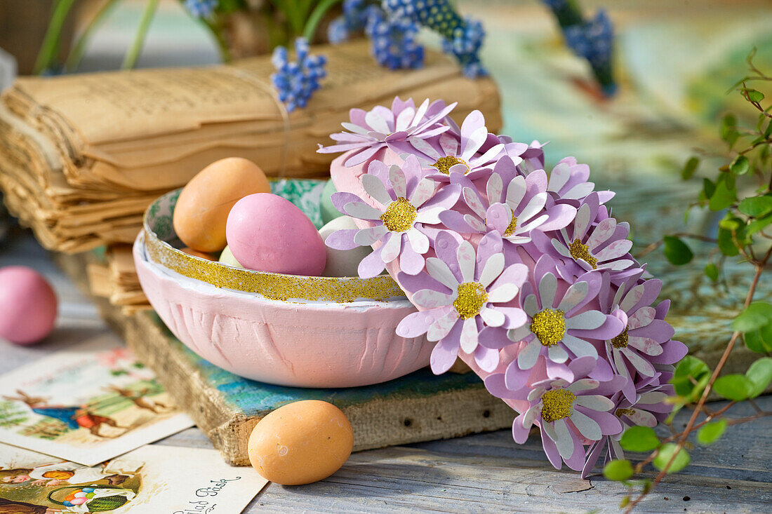Eiförmge Schale mit bunten Ostereiern und Deckel mit Papierblüten verziert