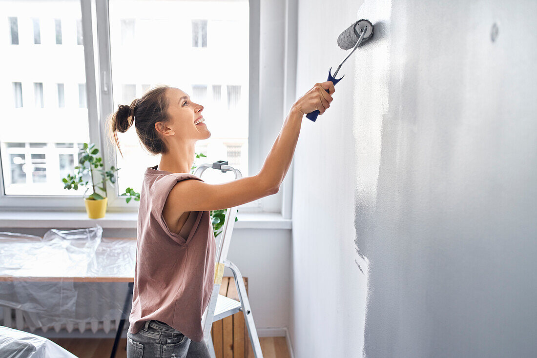 Lächelnde Frau, die Wand mit Farbroller malt