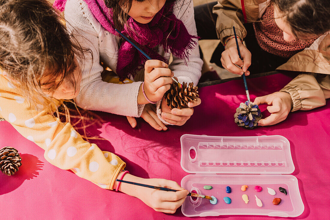 Mädchen mit Pinseln zum Färben von Tannenzapfen am Picknicktisch im Park an sonnigen Tagen